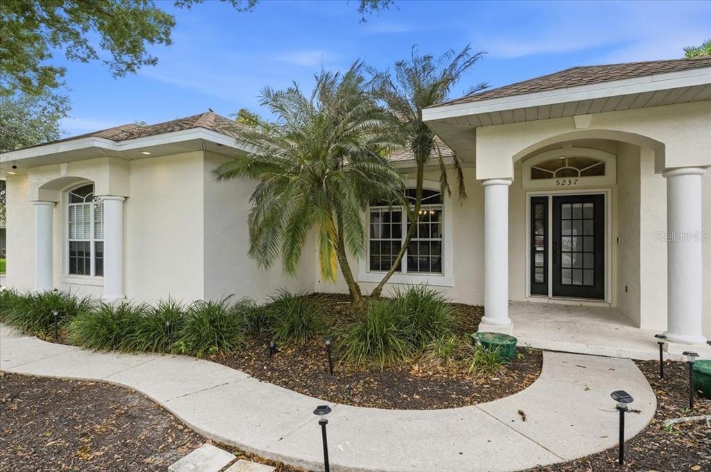 A single-story house exterior features a palm tree, white columns, and a curved walkway — 5237 BLOOMFIELD BOULEVARD, LAKELAND, FL