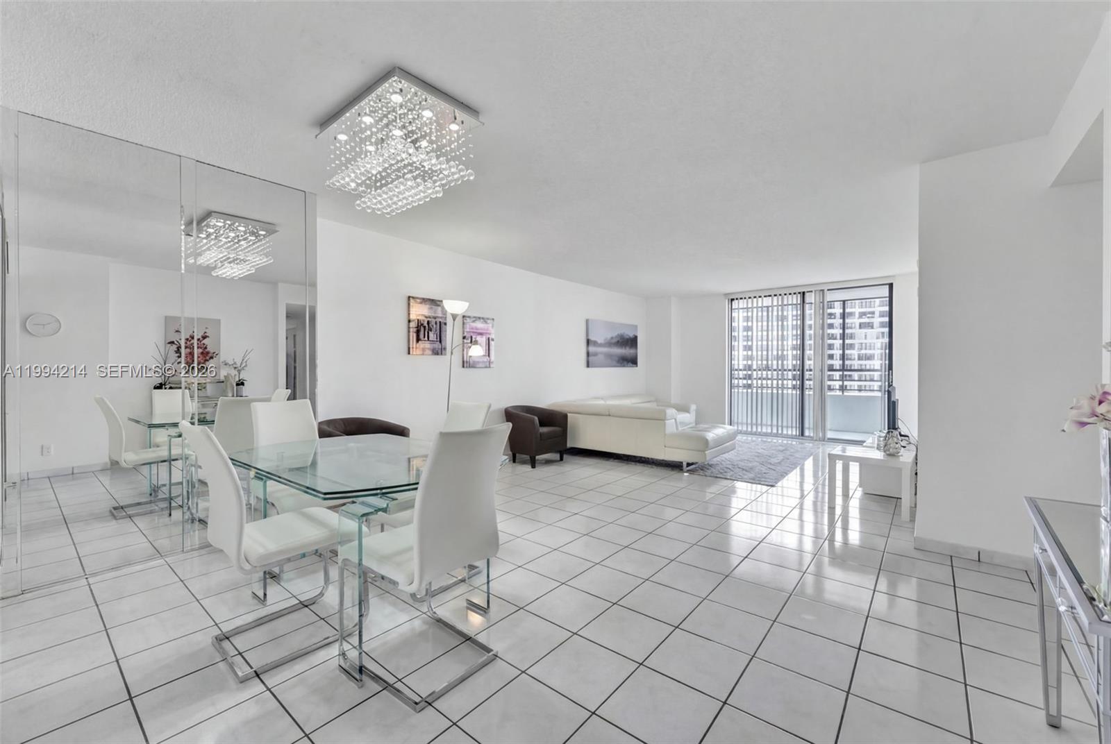 A bright, open-concept living and dining area features white tile floors and a crystal chandelier — 2500 PARKVIEW DR # 1418, Hallandale Beach FL 33009, HALLANDALE BEACH, FL