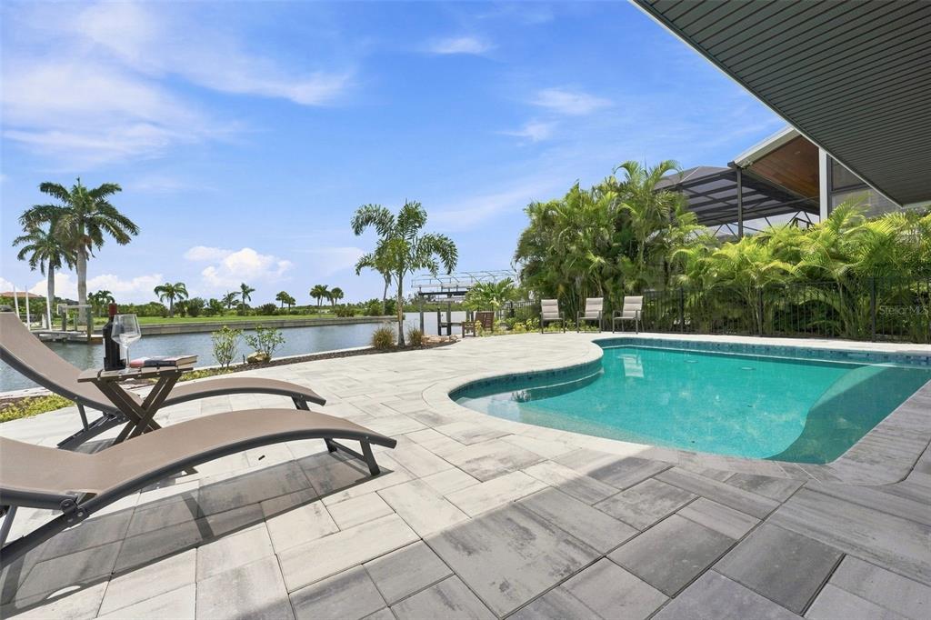 A swimming pool and lounge chairs sit on a patio overlooking a canal and palm trees — 2795 N BEACH ROAD UNIT B, ENGLEWOOD, FL