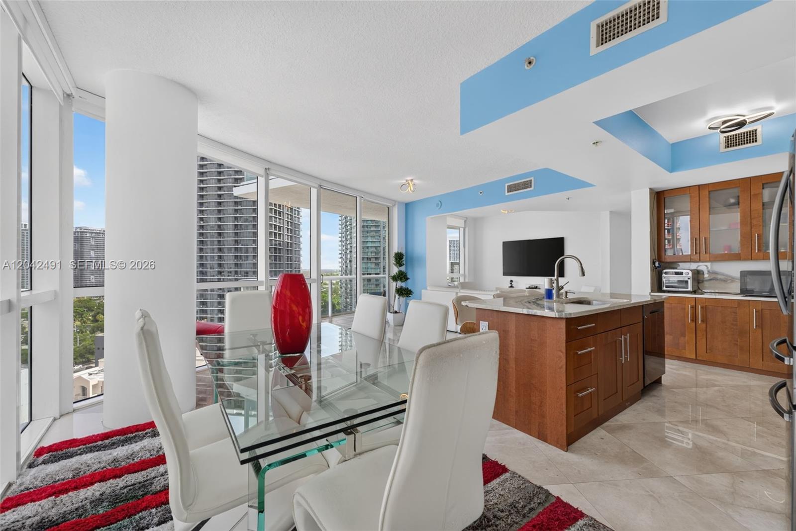 A dining area with a glass table and white chairs sits beside a kitchen island — 480 NE 30th St # 1807, Miami FL 33137, MIAMI, FL