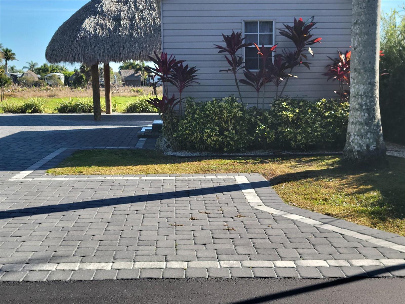 A paved driveway leads to a house with a thatched-roof structure in the background — 3704 SW 7th Manor, Okeechobee FL 34974, OKEECHOBEE, FL