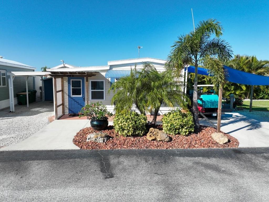 A single-story mobile home with a blue door, palm trees, and a gravel garden bed — 1475 FLAMINGO DRIVE UNIT 346, ENGLEWOOD, FL