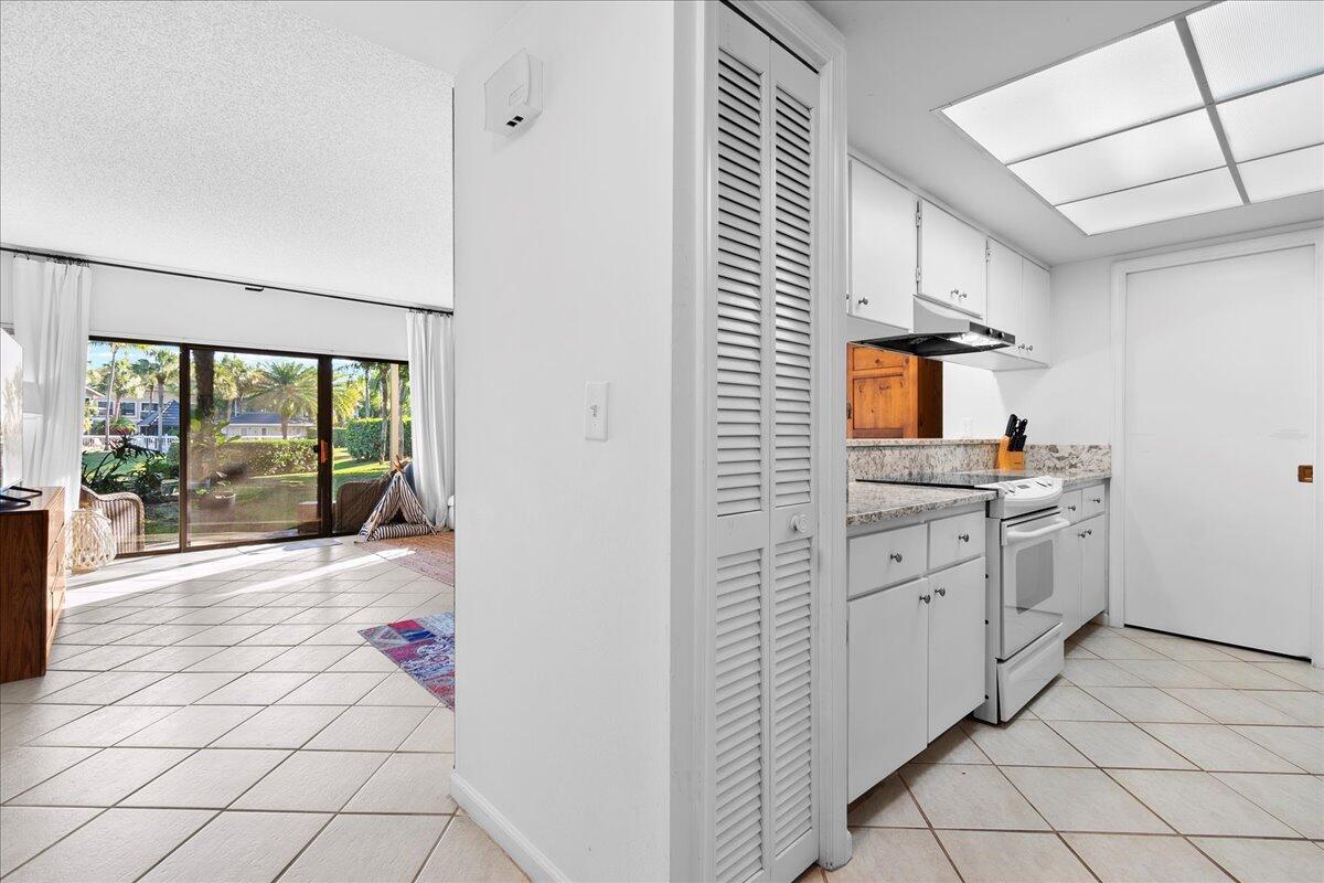 A kitchen with white cabinets and tile floors opens to a living area with sliding doors — 11863 Wimbledon Circle # 446, Wellington FL 33414, WELLINGTON, FL