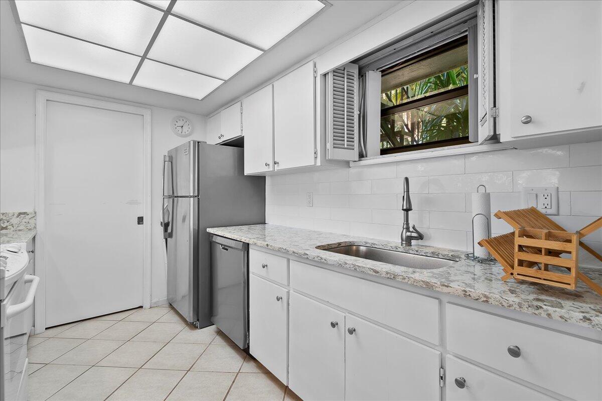 A kitchen features white cabinets, granite countertops, a stainless steel refrigerator, and a subway tile backsplash — 11863 Wimbledon Circle # 446, Wellington FL 33414, WELLINGTON, FL