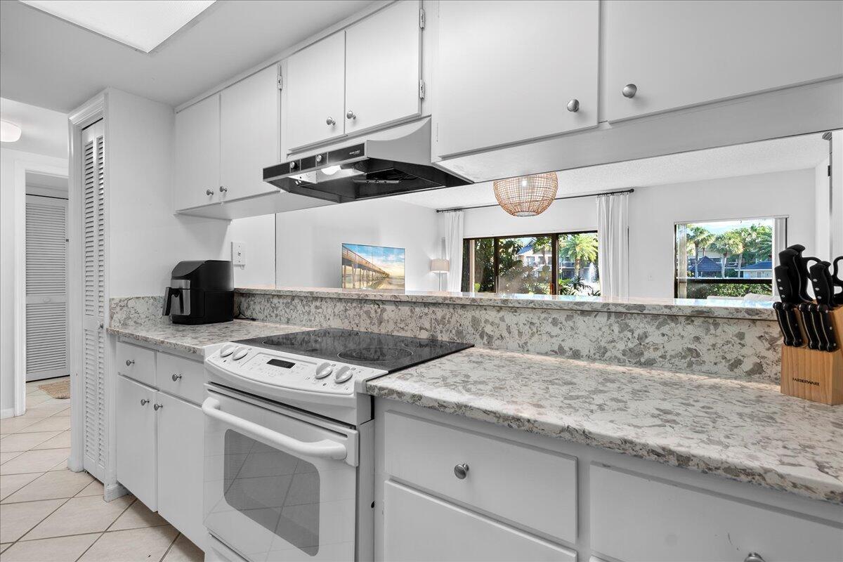 A white kitchen features speckled countertops, a glass cooktop, and a view into the living area — 11863 Wimbledon Circle # 446, Wellington FL 33414, WELLINGTON, FL