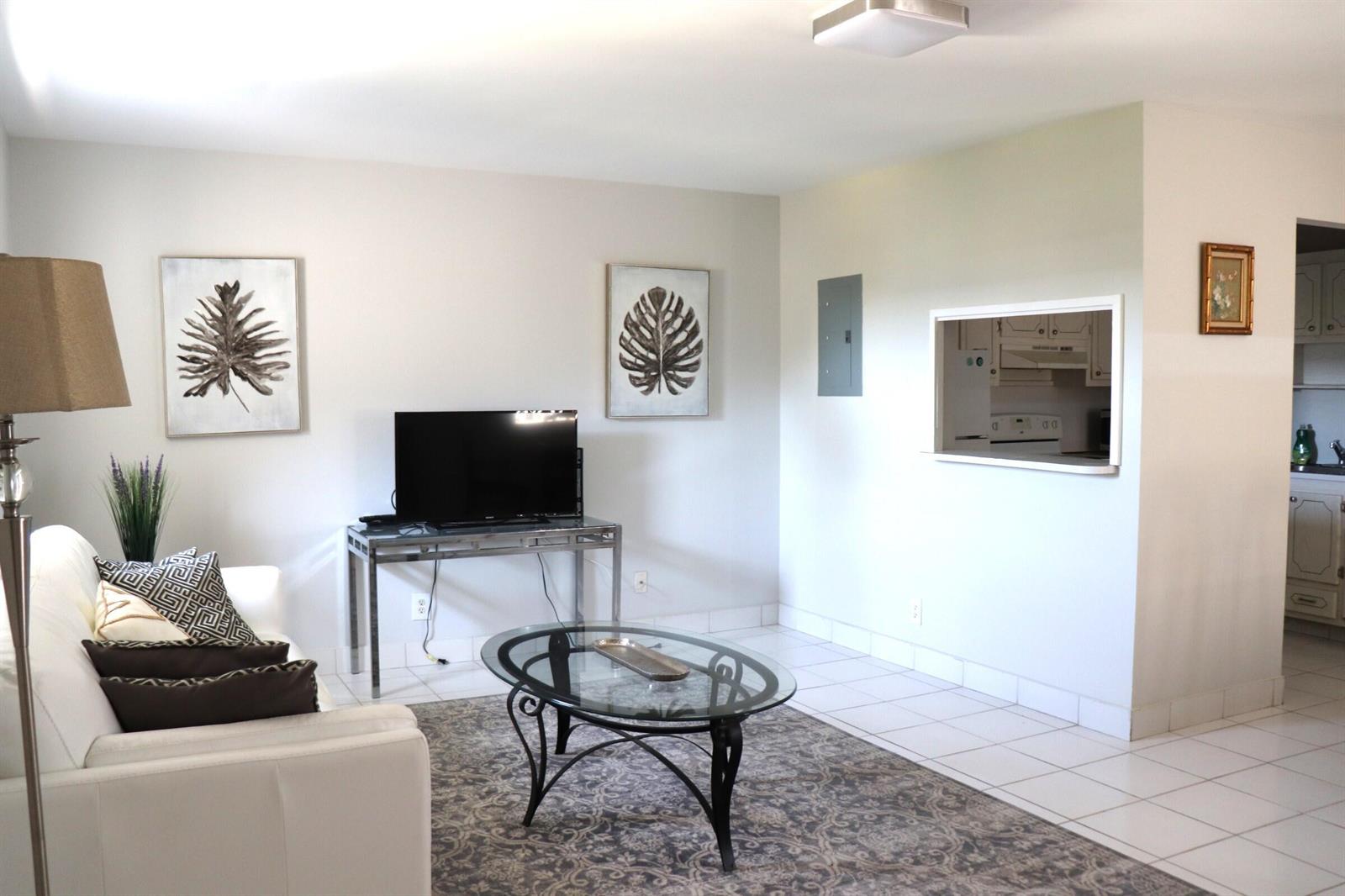 A living room with white walls, tile flooring, a white sofa, and a kitchen pass-through — 79 Brittany # B, Delray Beach FL 33446, DELRAY BEACH, FL
