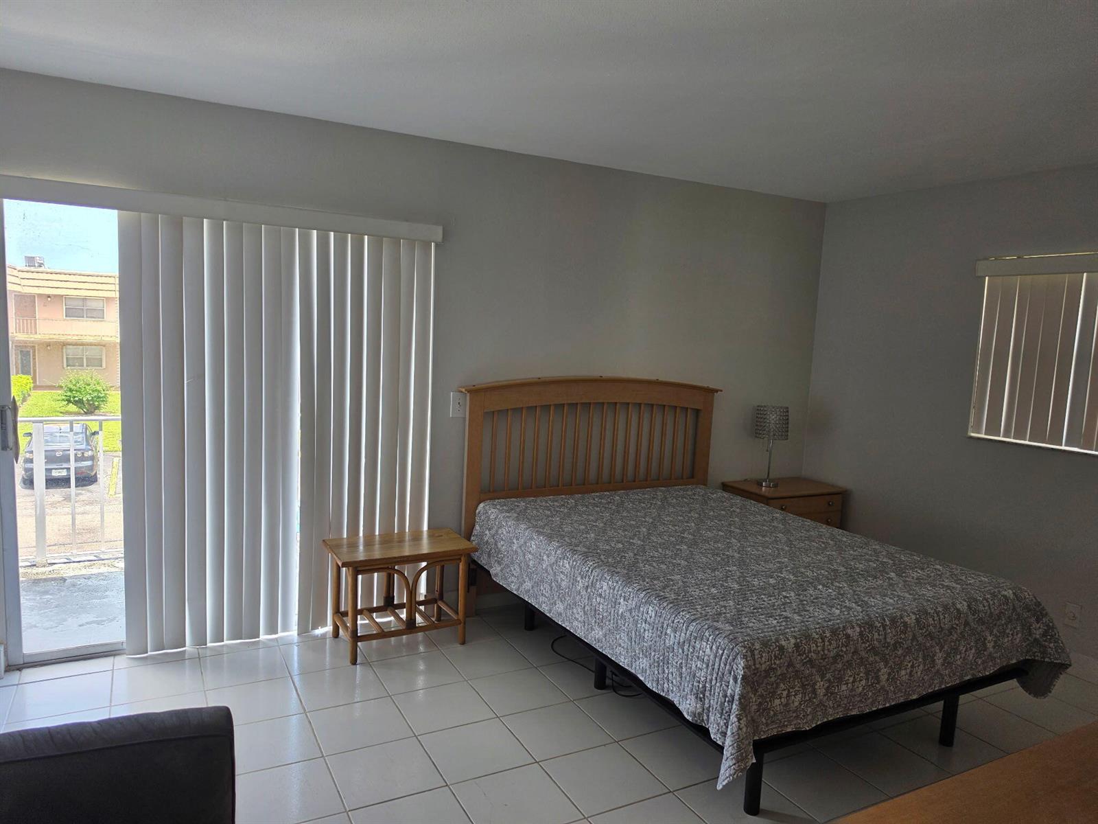 A bedroom with tile floors, a wooden bed frame, and a sliding glass door — 79 Brittany # B, Delray Beach FL 33446, DELRAY BEACH, FL