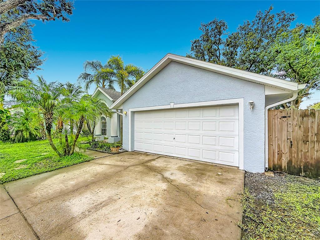 A light blue house exterior features a white two-car garage door and a concrete driveway — 6146 104TH AVENUE N, PINELLAS PARK, FL