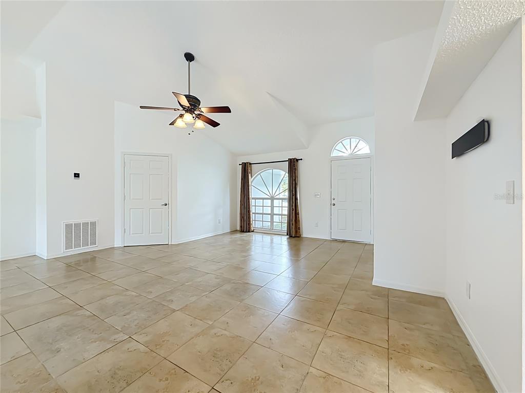 An empty room with beige tile flooring, a vaulted ceiling, a ceiling fan, and two doors — 6146 104TH AVENUE N, PINELLAS PARK, FL