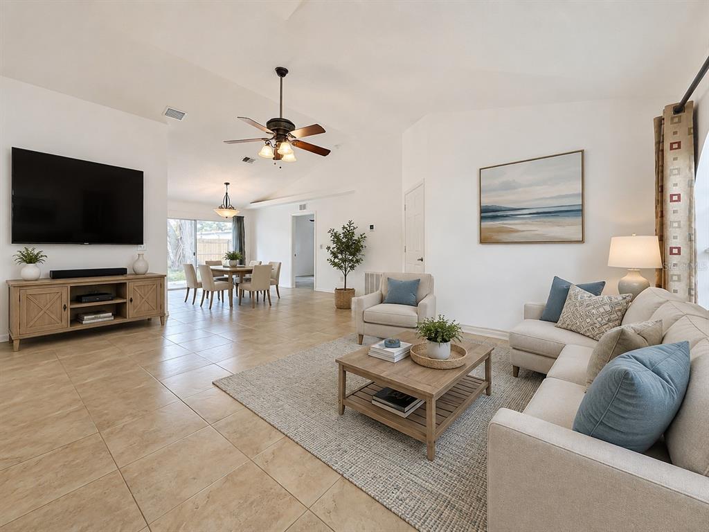 An open-concept living and dining area features tile flooring, a ceiling fan, and neutral furniture — 6146 104TH AVENUE N, PINELLAS PARK, FL