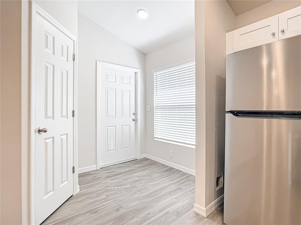 A kitchen area features light wood-look flooring, white doors, a window, and a stainless refrigerator — 17053 NIXON AVENUE, PORT CHARLOTTE, FL