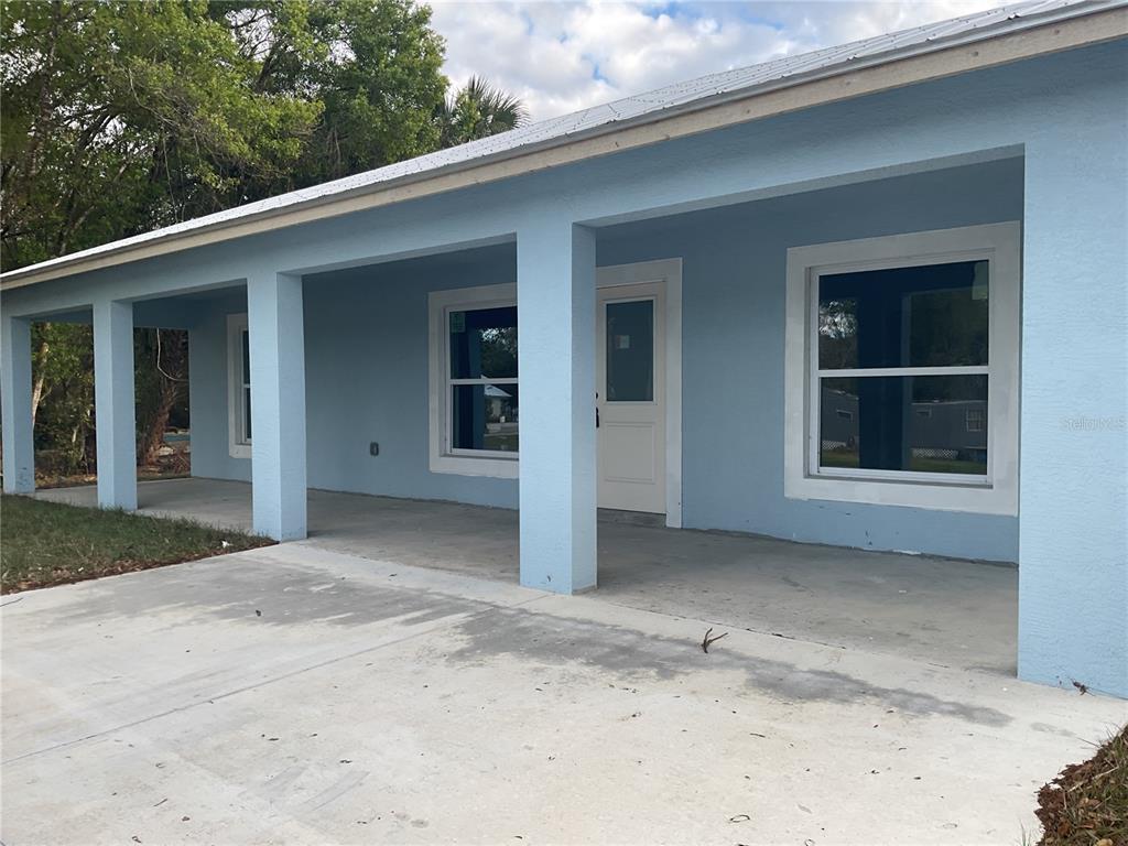 A light blue house features a covered front porch with concrete flooring and white trim — 2432 NW 5TH STREET, OKEECHOBEE, FL