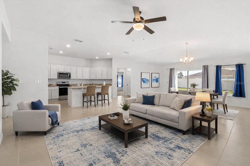 A bright open-concept living room and kitchen featuring white cabinetry, tile floors, and neutral furniture — 1429 MATTIE POINTE LANE, AUBURNDALE, FL