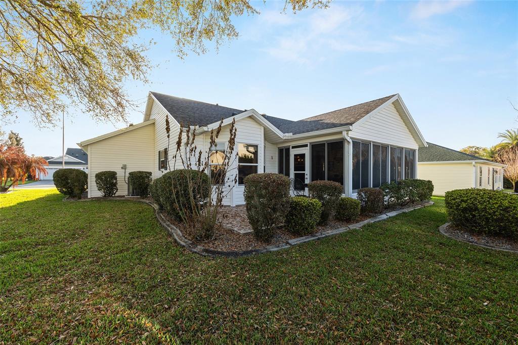 The rear exterior of a single-story house features a screened-in porch and landscaped bushes — 624 FAYETTE COURT, THE VILLAGES, FL