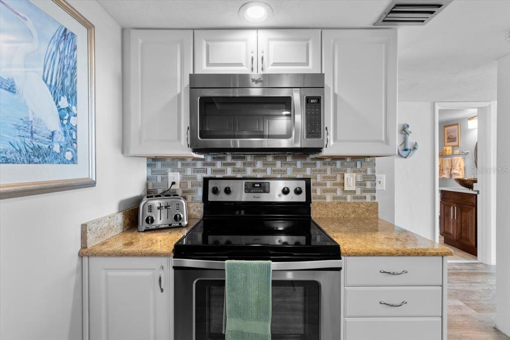 A kitchen features white cabinets, stainless steel appliances, a tiled backsplash, and granite countertops — 3855 S ATLANTIC AVENUE UNIT PH5, DAYTONA BEACH SHORES, FL