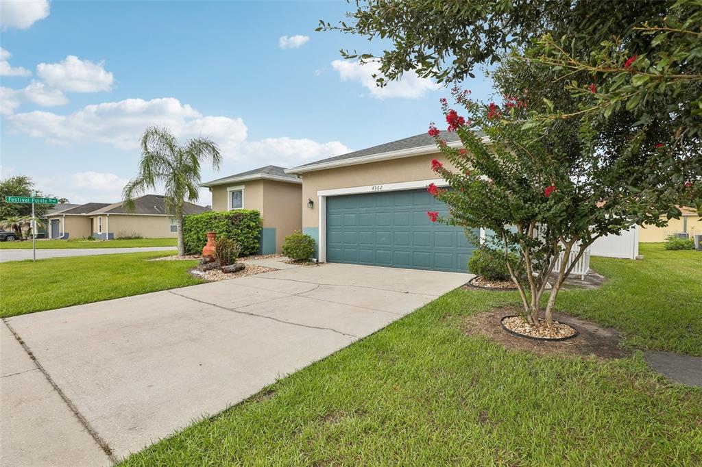 A single-story house with a teal garage door, concrete driveway, and a blooming crepe myrtle — 4362 SUN CENTER ROAD, MULBERRY, FL