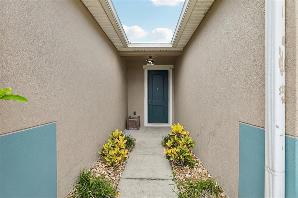 A concrete walkway leads to a dark blue front door framed by two stucco walls — 4362 SUN CENTER ROAD, MULBERRY, FL