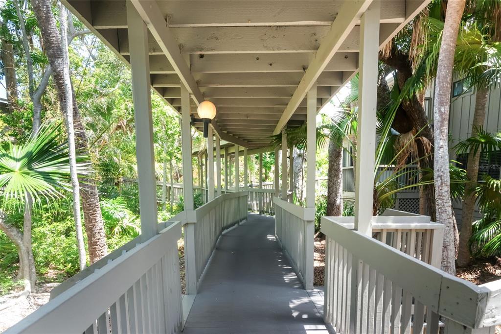 A covered wooden walkway with railings winds through a lush, tropical outdoor setting — 1347 LANDINGS DRIVE UNIT 6, SARASOTA, FL