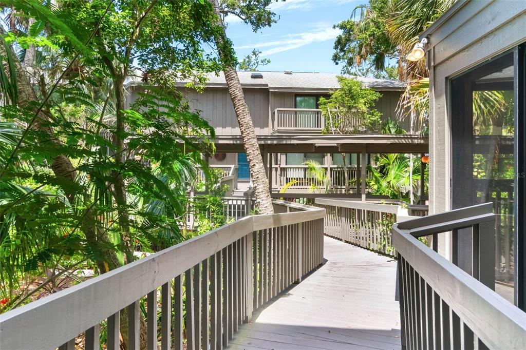 A wooden walkway leads toward a multi-story building surrounded by lush green trees and foliage — 1347 LANDINGS DRIVE UNIT 6, SARASOTA, FL