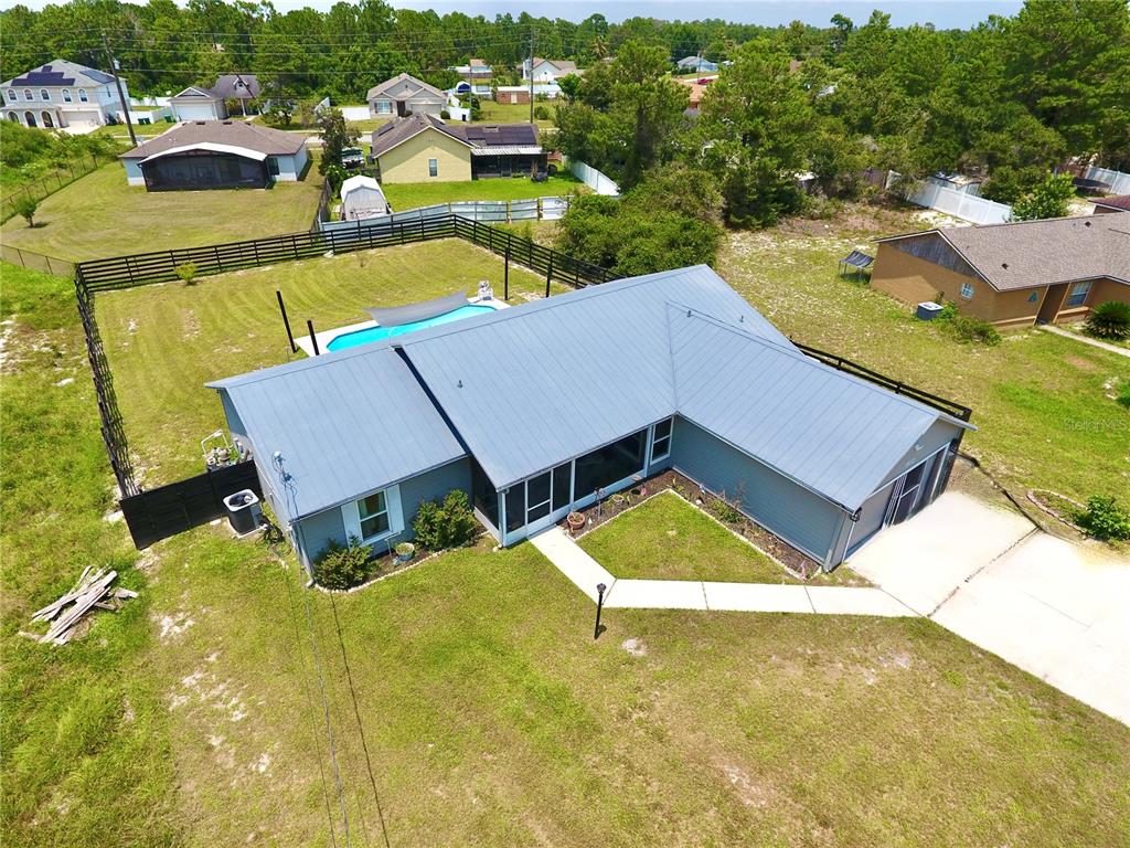 An aerial view shows a blue house with a metal roof, pool, and fenced yard — 1812 WHIPPLE DRIVE, DELTONA, FL