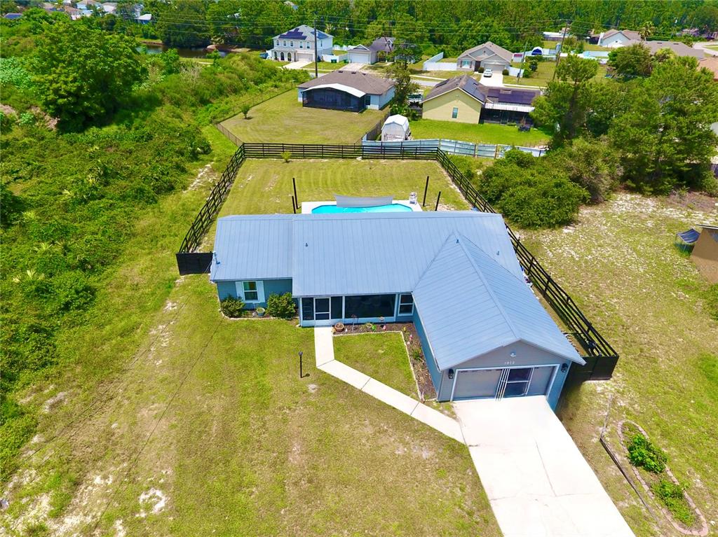 An aerial view shows a blue house with a metal roof, a pool, and a fenced yard — 1812 WHIPPLE DRIVE, DELTONA, FL