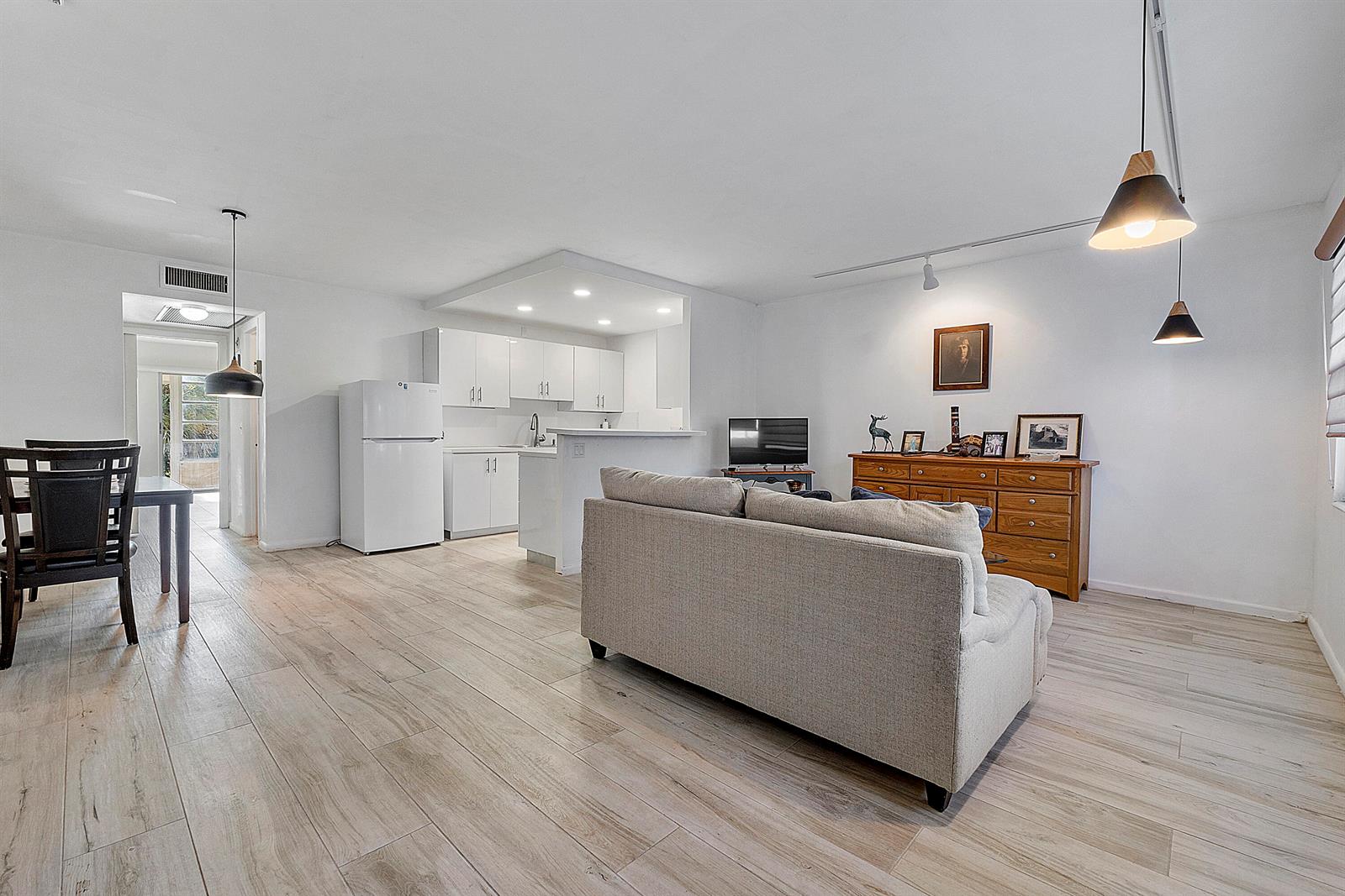 An open-concept living room and kitchen feature light wood-look flooring and white cabinetry — 1012 Newport G, Deerfield Beach FL 33442, DEERFIELD BEACH, FL