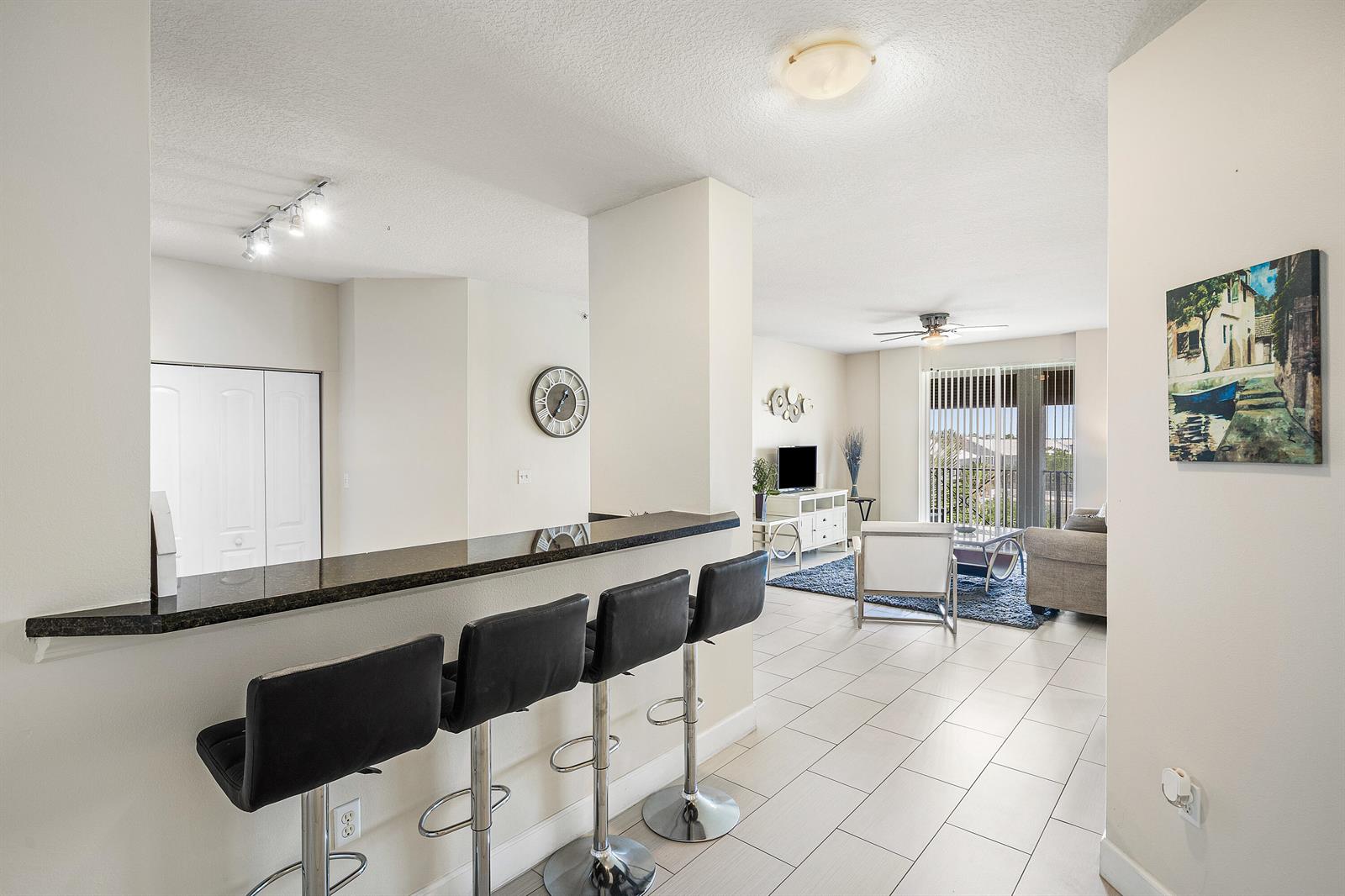 A kitchen breakfast bar with black stools overlooks a living area with tile flooring — 255 NE 3rd Avenue # 2503, Delray Beach FL 33444, DELRAY BEACH, FL