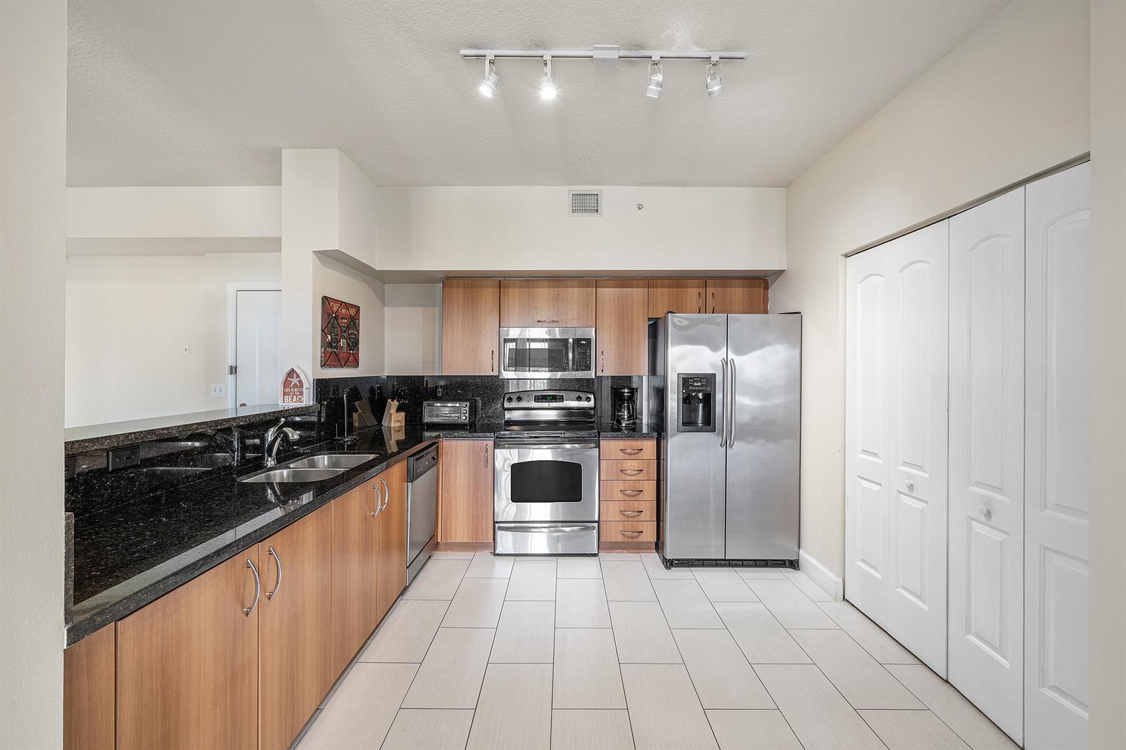 A kitchen features wood cabinets, black granite countertops, stainless steel appliances, and white tile flooring — 255 NE 3rd Avenue # 2503, Delray Beach FL 33444, DELRAY BEACH, FL