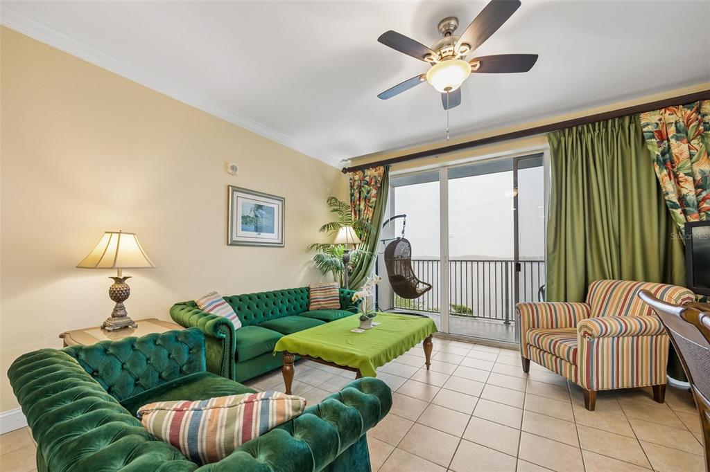 A living room features green tufted sofas, a striped armchair, and a balcony overlooking water — 13415 BLUE HERON BEACH DRIVE UNIT 610, ORLANDO, FL