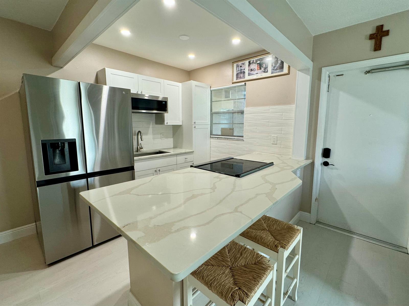 A kitchen features white cabinets, stainless steel appliances, a quartz island, and two woven stools — 30 S J Street # 16, FL 33460, FL