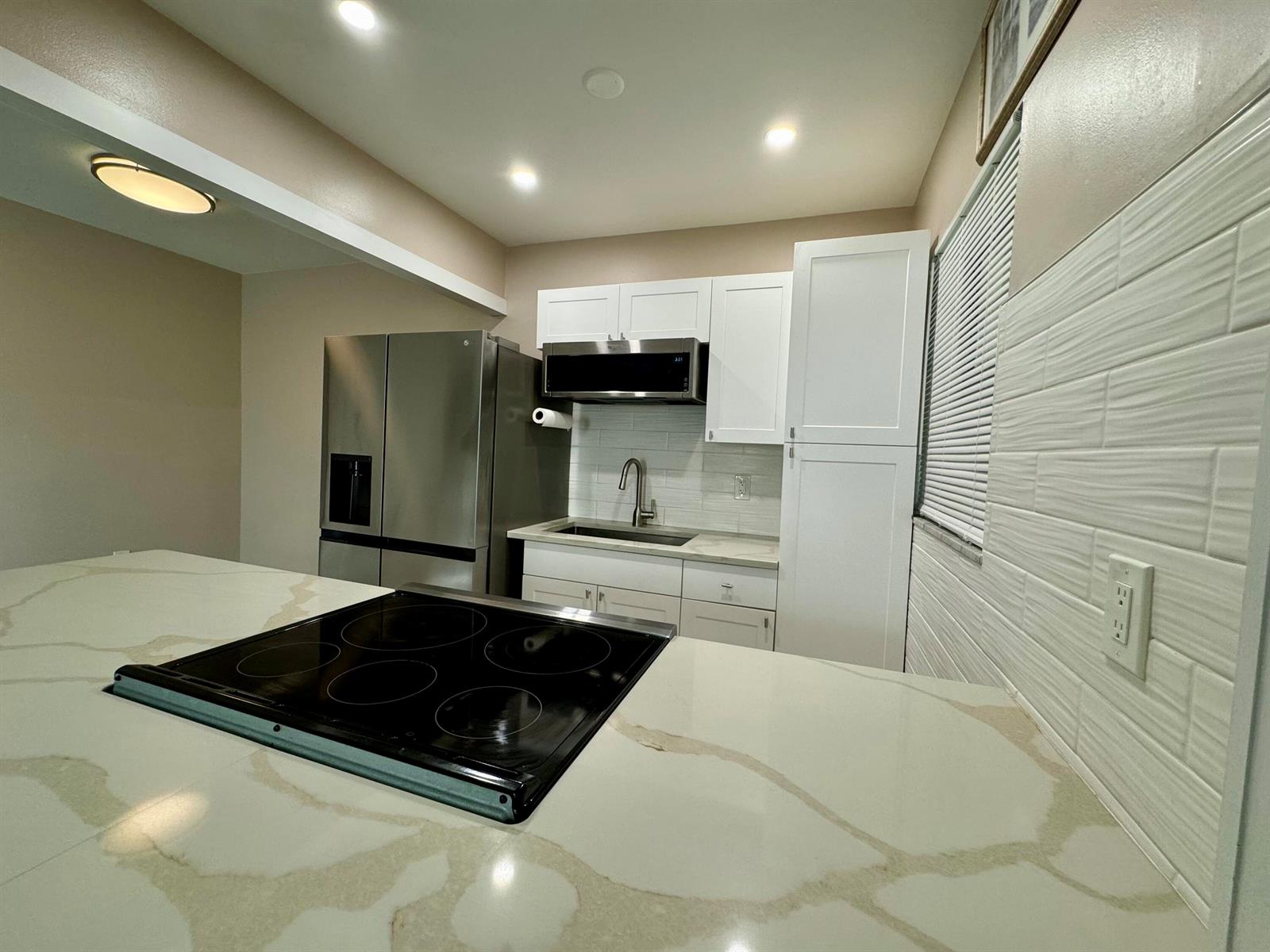 A kitchen features white cabinets, stainless steel appliances, and a quartz countertop with a cooktop — 30 S J Street # 16, FL 33460, FL