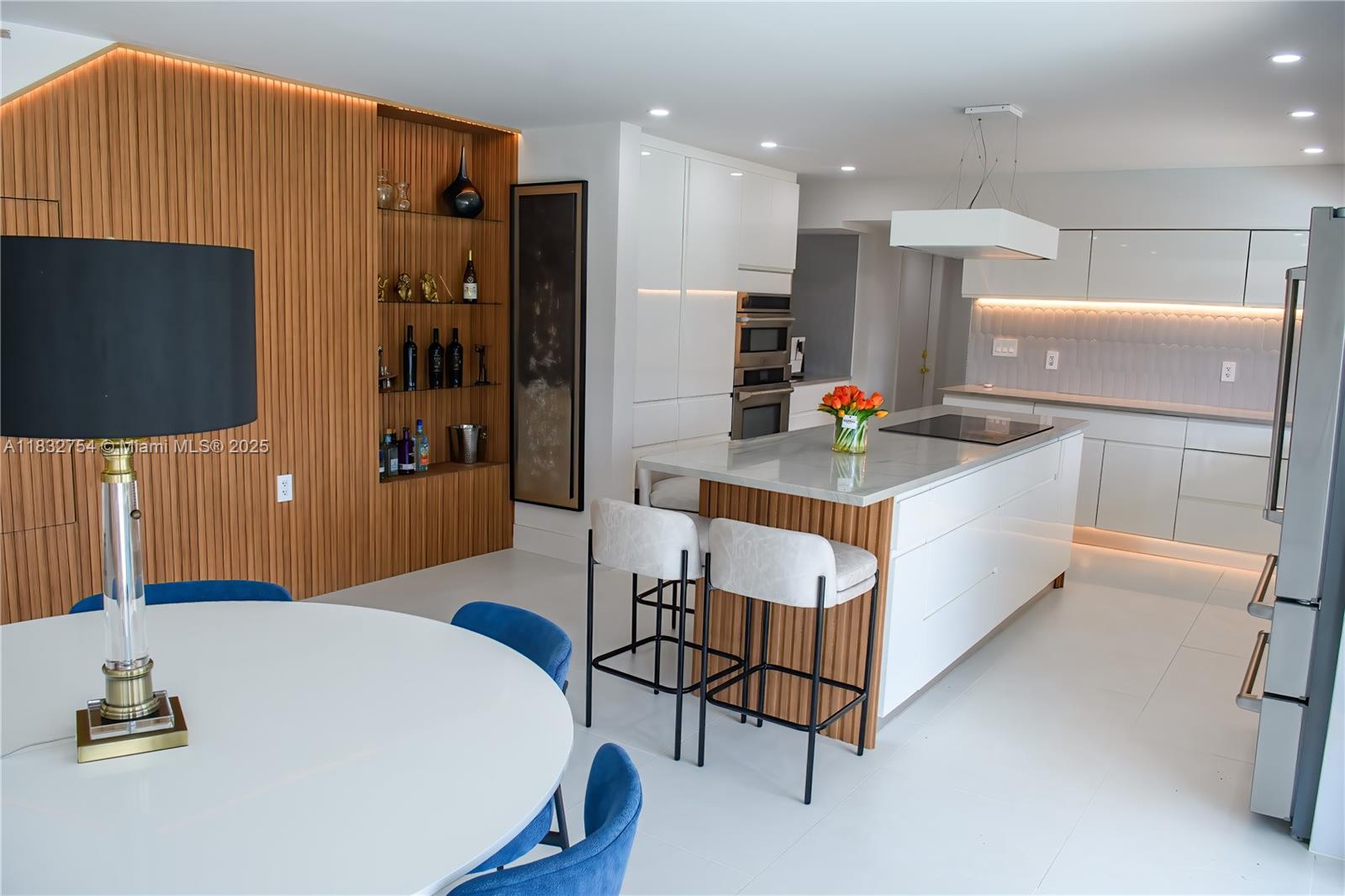 A modern kitchen and dining area features white cabinetry, a wood-slatted accent wall, and an island — 1240 NE 27th Ter, Pompano Beach FL 33062, POMPANO BEACH, FL