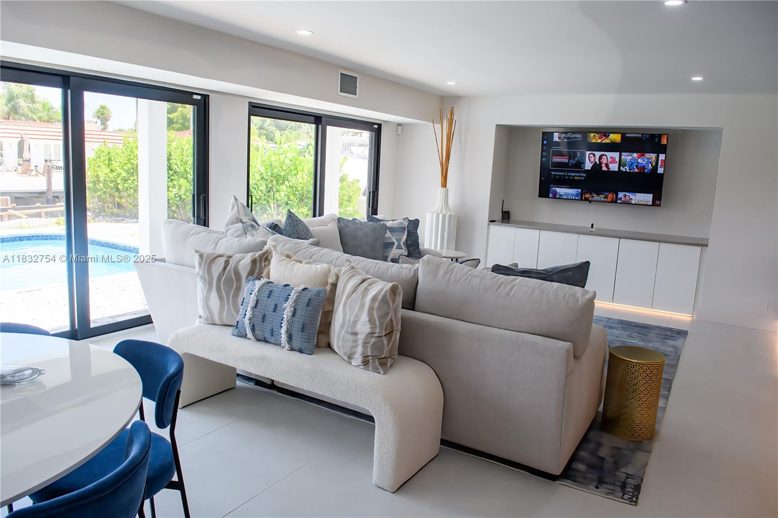 A modern living room features a large sectional sofa, built-in media cabinetry, and sliding glass doors — 1240 NE 27th Ter, Pompano Beach FL 33062, POMPANO BEACH, FL