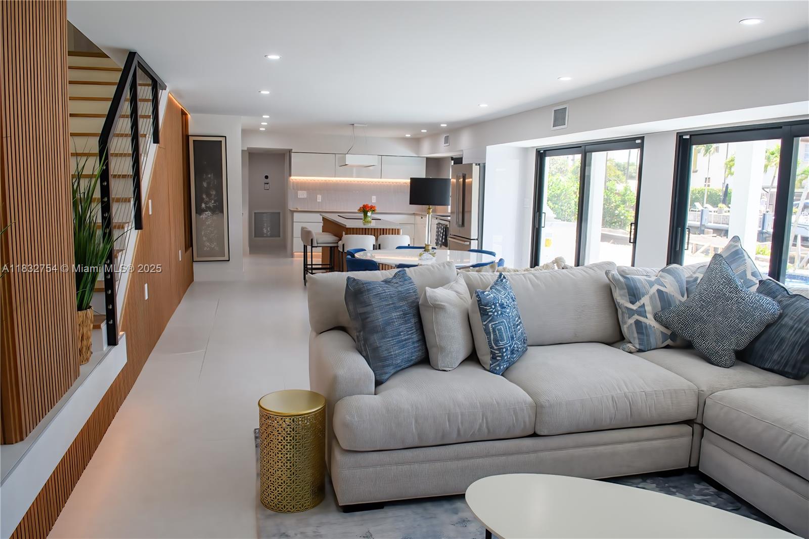 A modern open-concept living area features a sectional sofa, a kitchen, and a wooden staircase — 1240 NE 27th Ter, Pompano Beach FL 33062, POMPANO BEACH, FL