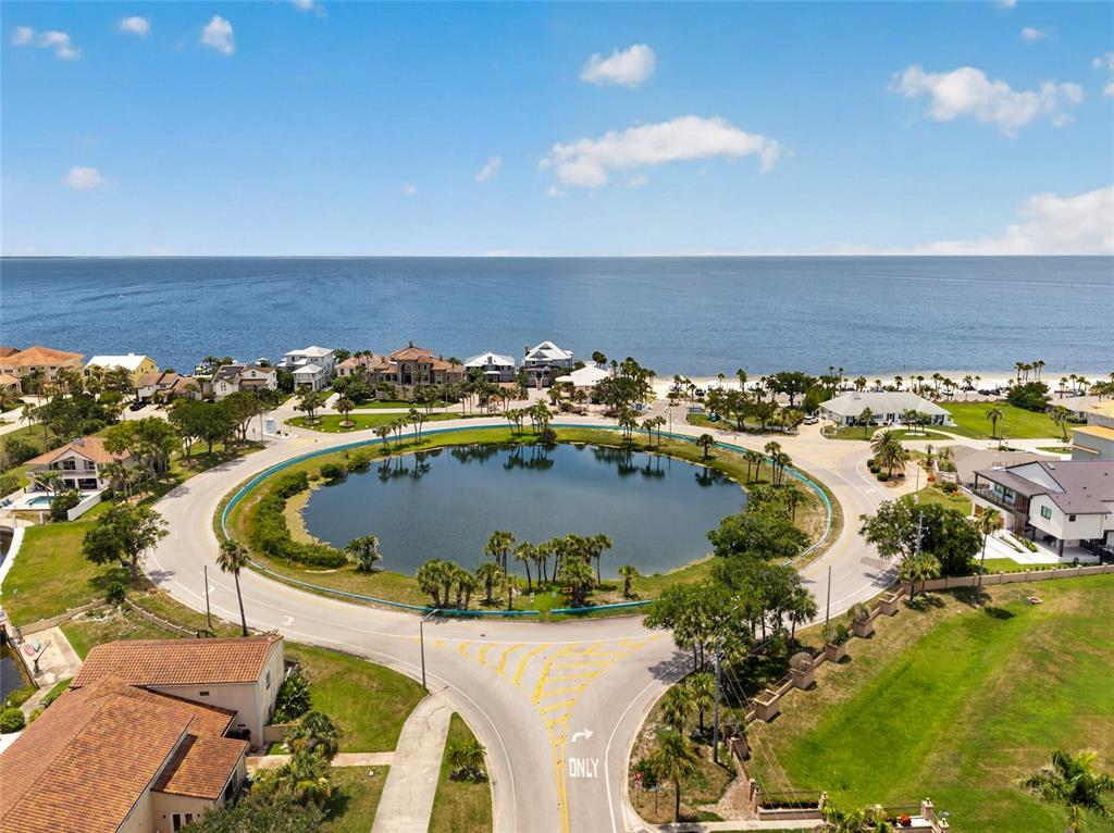 An aerial view shows a circular road surrounding a pond near a coastal beach — 6420 BANYAN BOULEVARD UNIT 201, NEW PORT RICHEY, FL