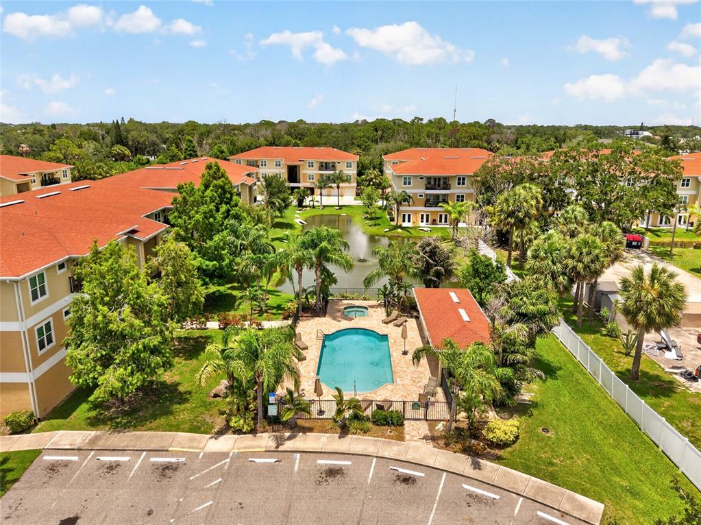 An aerial view shows apartment buildings surrounding a central swimming pool and a small pond — 6420 BANYAN BOULEVARD UNIT 201, NEW PORT RICHEY, FL