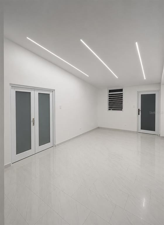 A bright, minimalist room features white tile floors, recessed linear ceiling lights, and two doors — . 26 UNIT M25, CAROLINA, PR