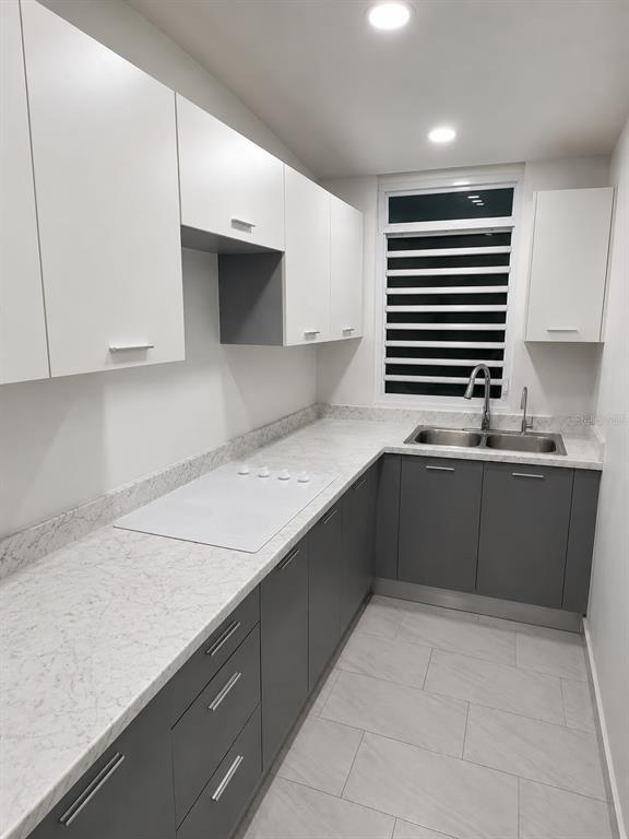 A modern kitchen features white upper cabinets, gray lower cabinets, and white marble-patterned countertops — . 26 UNIT M25, CAROLINA, PR