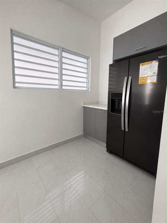 A kitchen area features a black refrigerator, grey cabinets, and light-colored tile flooring — . 26 UNIT M25, CAROLINA, PR