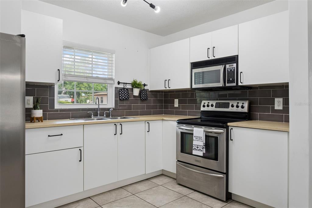 A kitchen with white cabinets, stainless steel appliances, light wood countertops, and gray subway tile — 8303 TEMPLE PARK DRIVE, TAMPA, FL