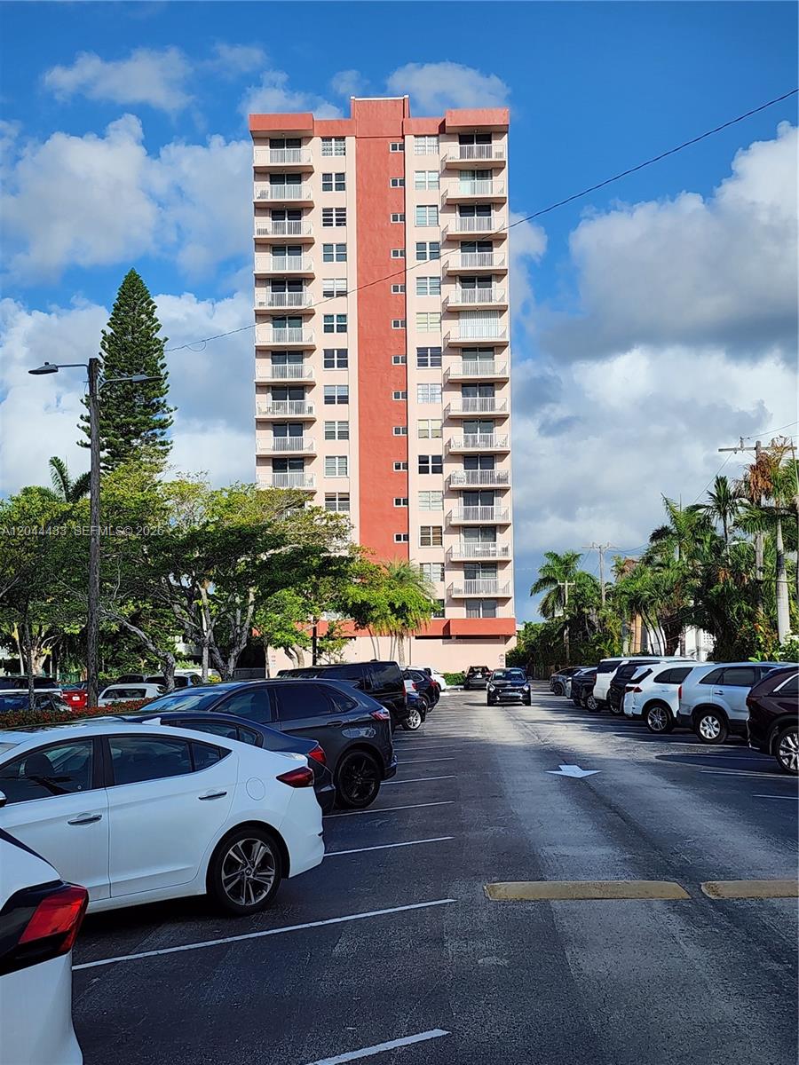 A tall, multi-story residential apartment building stands behind a parking lot filled with cars — 3161 S Ocean Dr # 404, Hallandale Beach FL 33009, HALLANDALE BEACH, FL