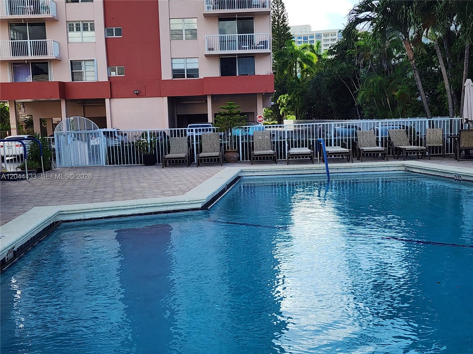 A swimming pool sits in front of a multi-story apartment building with patio chairs — 3161 S Ocean Dr # 404, Hallandale Beach FL 33009, HALLANDALE BEACH, FL