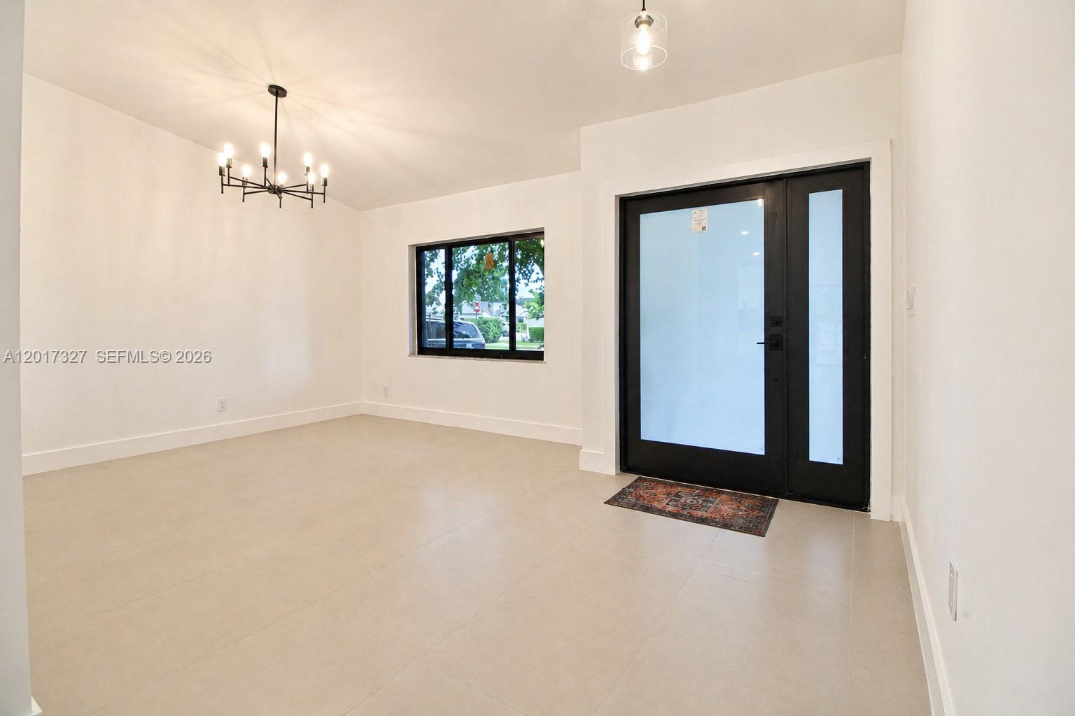 An empty room features white walls, light tile flooring, a modern chandelier, and a black-framed door — 10088 SW 143rd Ct, Miami FL 33186, MIAMI, FL