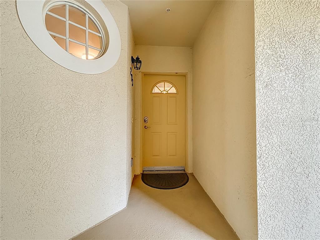 A yellow front door is centered at the end of a covered entryway with stucco walls — 960 COOPER STREET UNIT 203, VENICE, FL