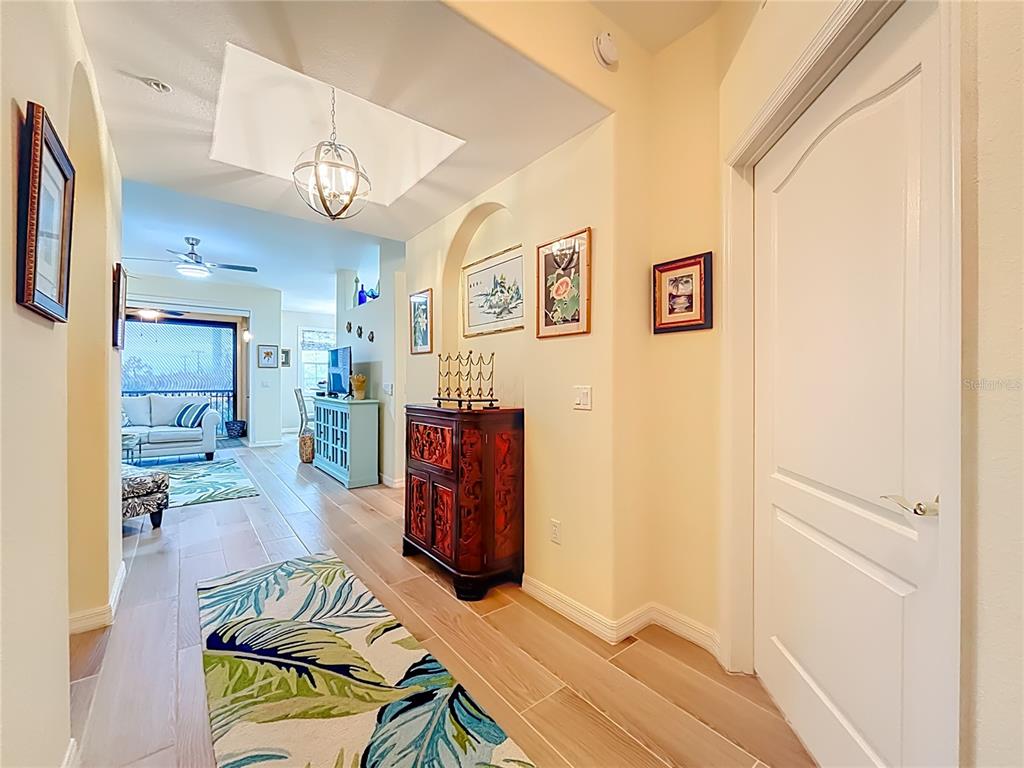 A hallway with light wood-look tile flooring leads toward a living area with a ceiling fan — 960 COOPER STREET UNIT 203, VENICE, FL