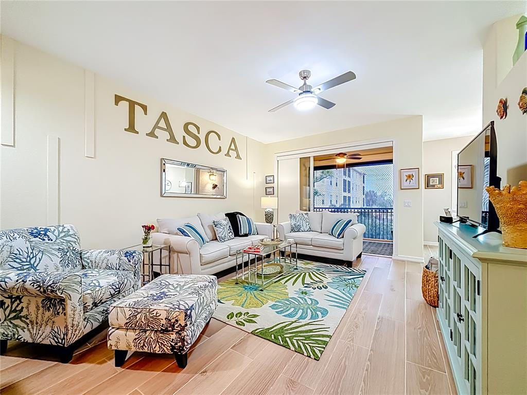 A living room features a patterned armchair, two white sofas, a tropical rug, and a balcony — 960 COOPER STREET UNIT 203, VENICE, FL