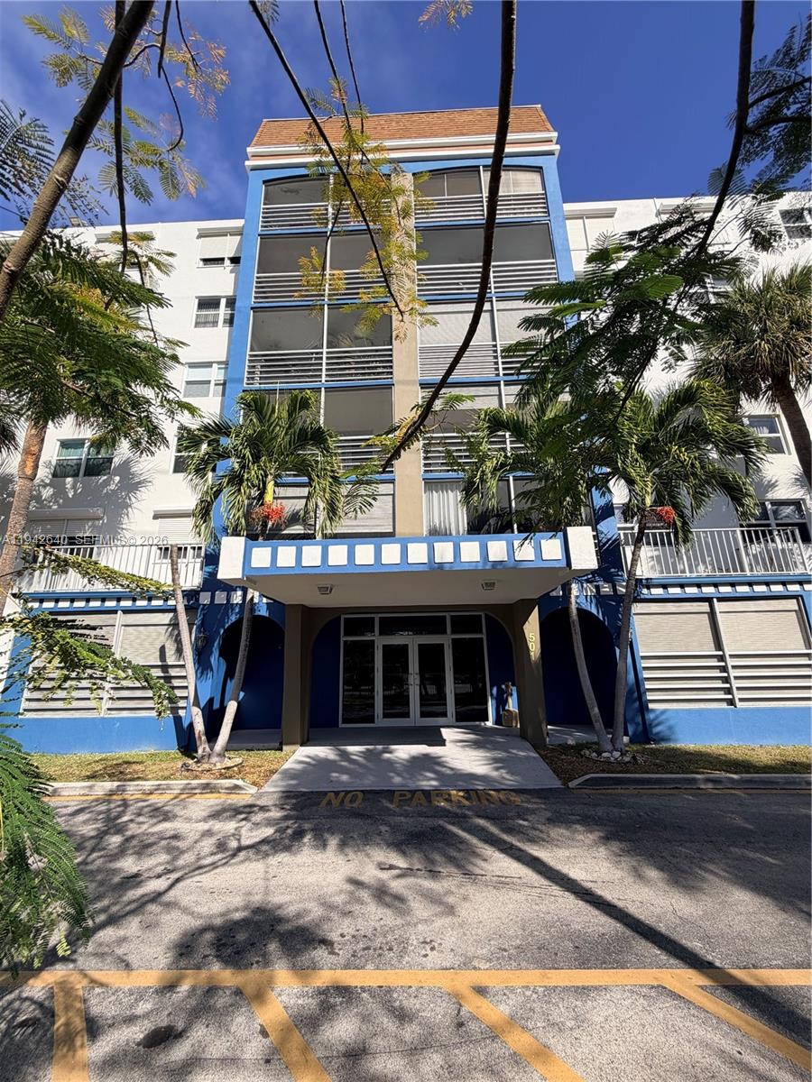 Exterior view of a multi-story apartment building with a blue entrance and palm trees — 501 E Dania Beach Blvd # 1B, Dania Beach FL 33004, DANIA BEACH, FL