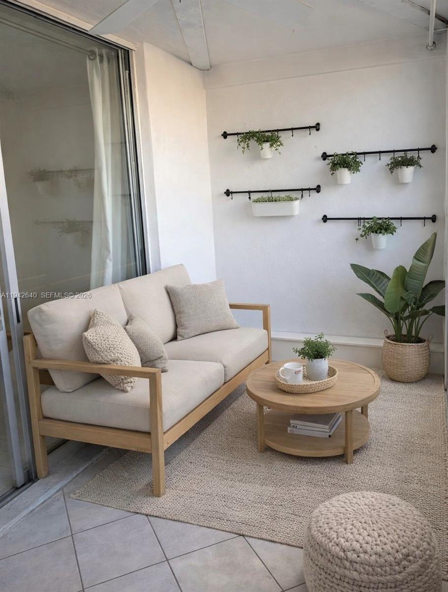 A balcony features a light-colored sofa, a round wooden coffee table, and wall-mounted hanging plants — 501 E Dania Beach Blvd # 1B, Dania Beach FL 33004, DANIA BEACH, FL