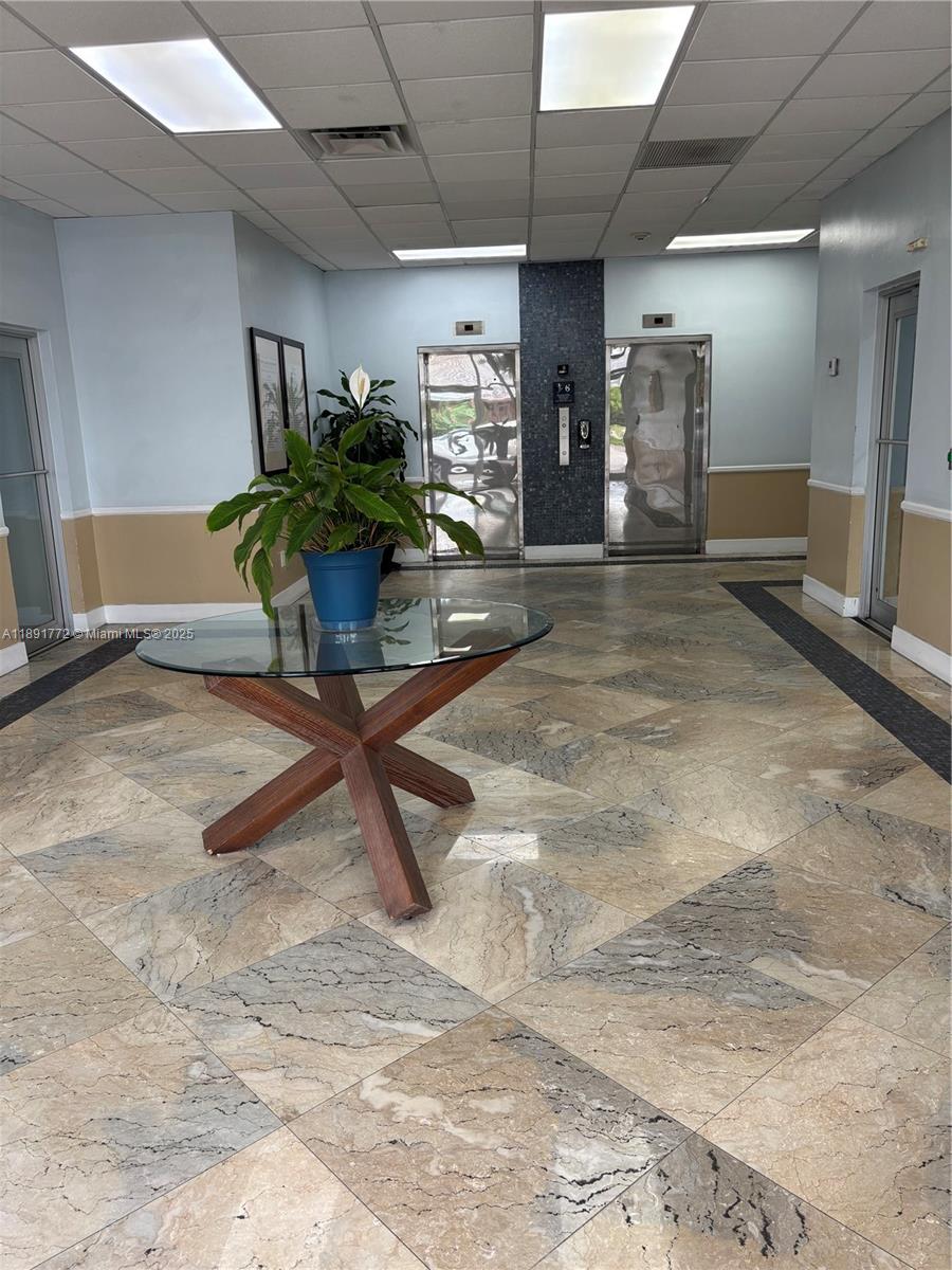 A lobby features a glass-topped table, a potted plant, and two elevators with tiled floors — 717 Ponce De Leon Blvd # 328, Coral Gables FL 33134, CORAL GABLES, FL