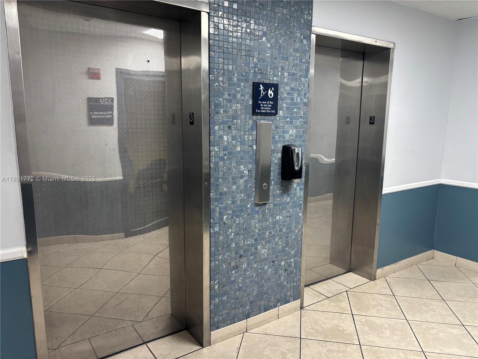 Two stainless steel elevators are set into a wall covered with blue mosaic tiles — 717 Ponce De Leon Blvd # 328, Coral Gables FL 33134, CORAL GABLES, FL